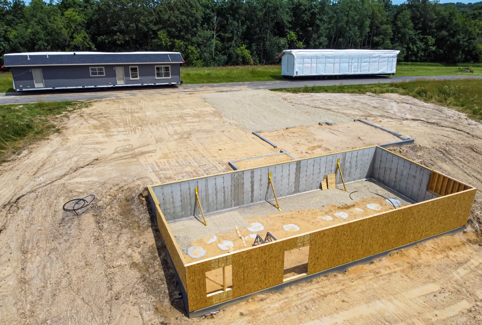 Modular home sections beside a freshly poured foundation